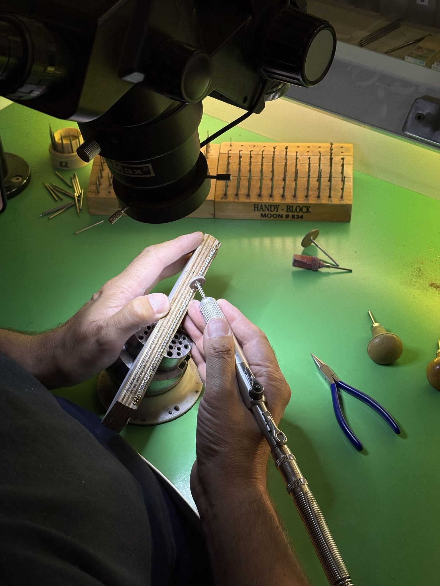Diamond setter at work under a stereo microscope, burs and tools at hand — SKJ Serti workshop, Antwerp